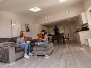Wide angle of hup! home extension with two sisters sitting with family dog